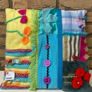 Zacht dementie kussen met verschillende texturen en speelse elementen, ontworpen om rust te bieden en zintuiglijke prikkels te stimuleren voor mensen met dementie.